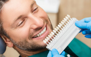 man in dental chair with strip of different color dental veneers in front of him.
