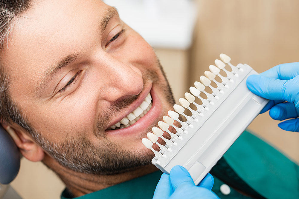 man in dental chair with strip of different color dental veneers in front of him.