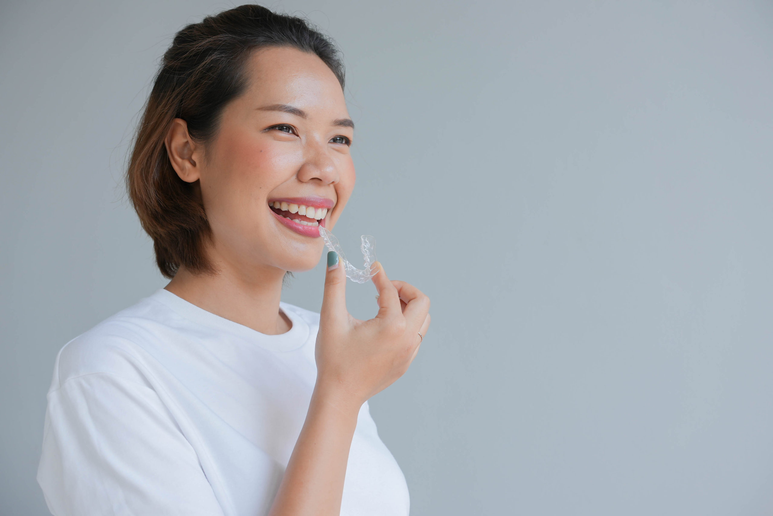 close up of a young asian woman smiling with Invisalign in her hand