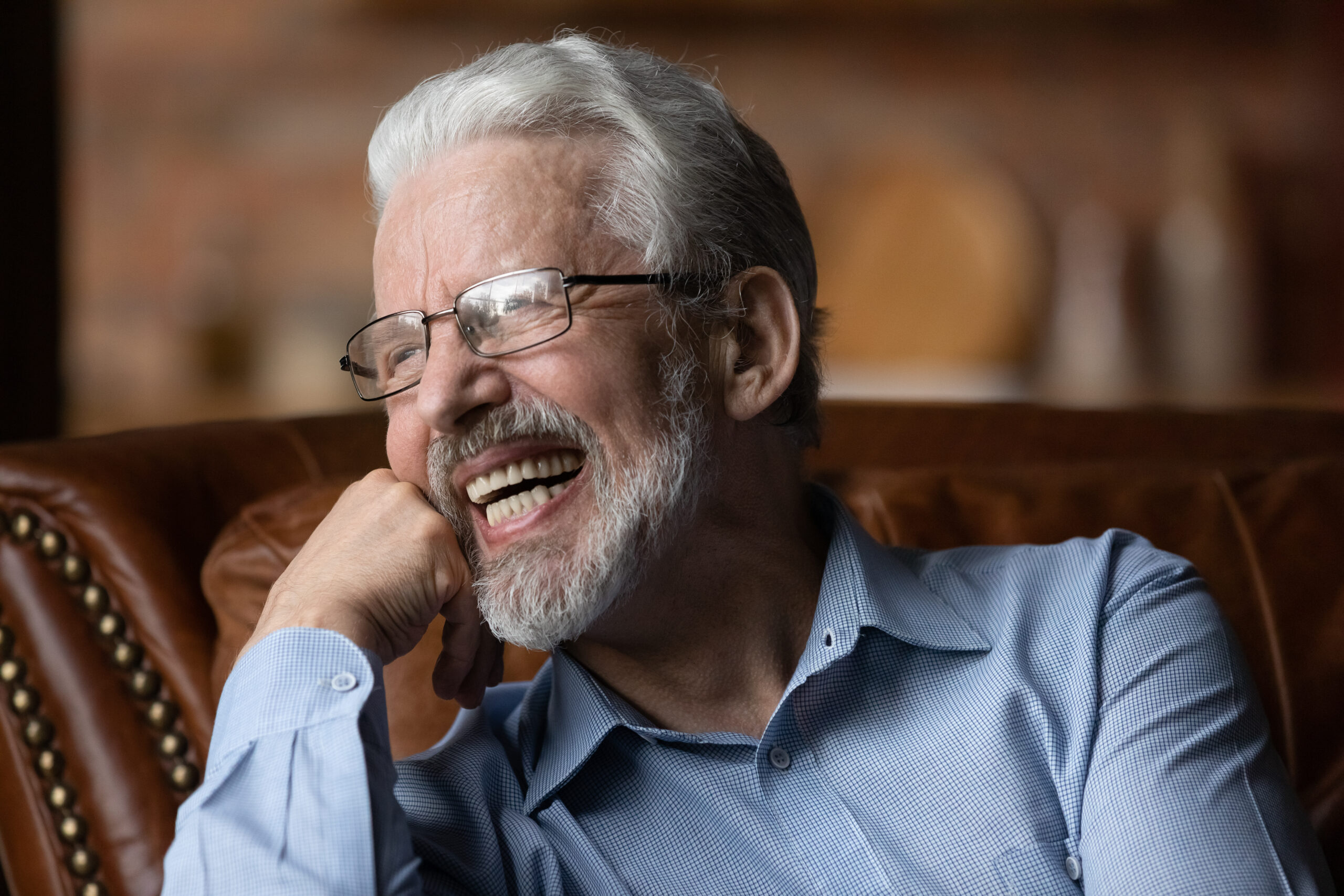 Older man with gray hair and glasses smiling and showing off dental implants