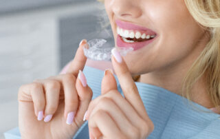 close up of a woman holding an invisalign tray while sitting in a dental chair