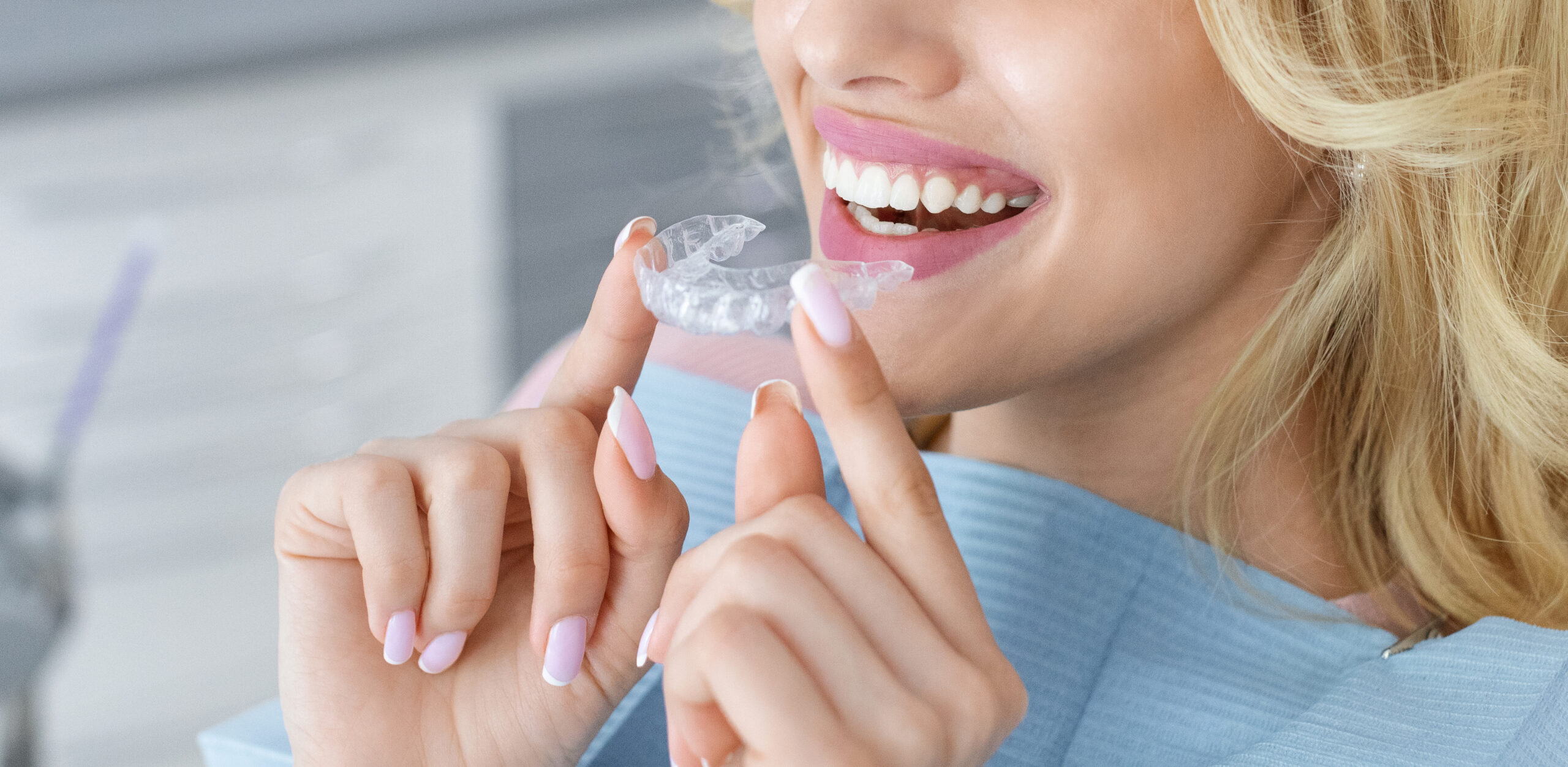 close up of a woman holding an invisalign tray while sitting in a dental chair