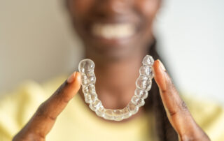 Young woman holding with two fingers an invisible dental aligner while smiling