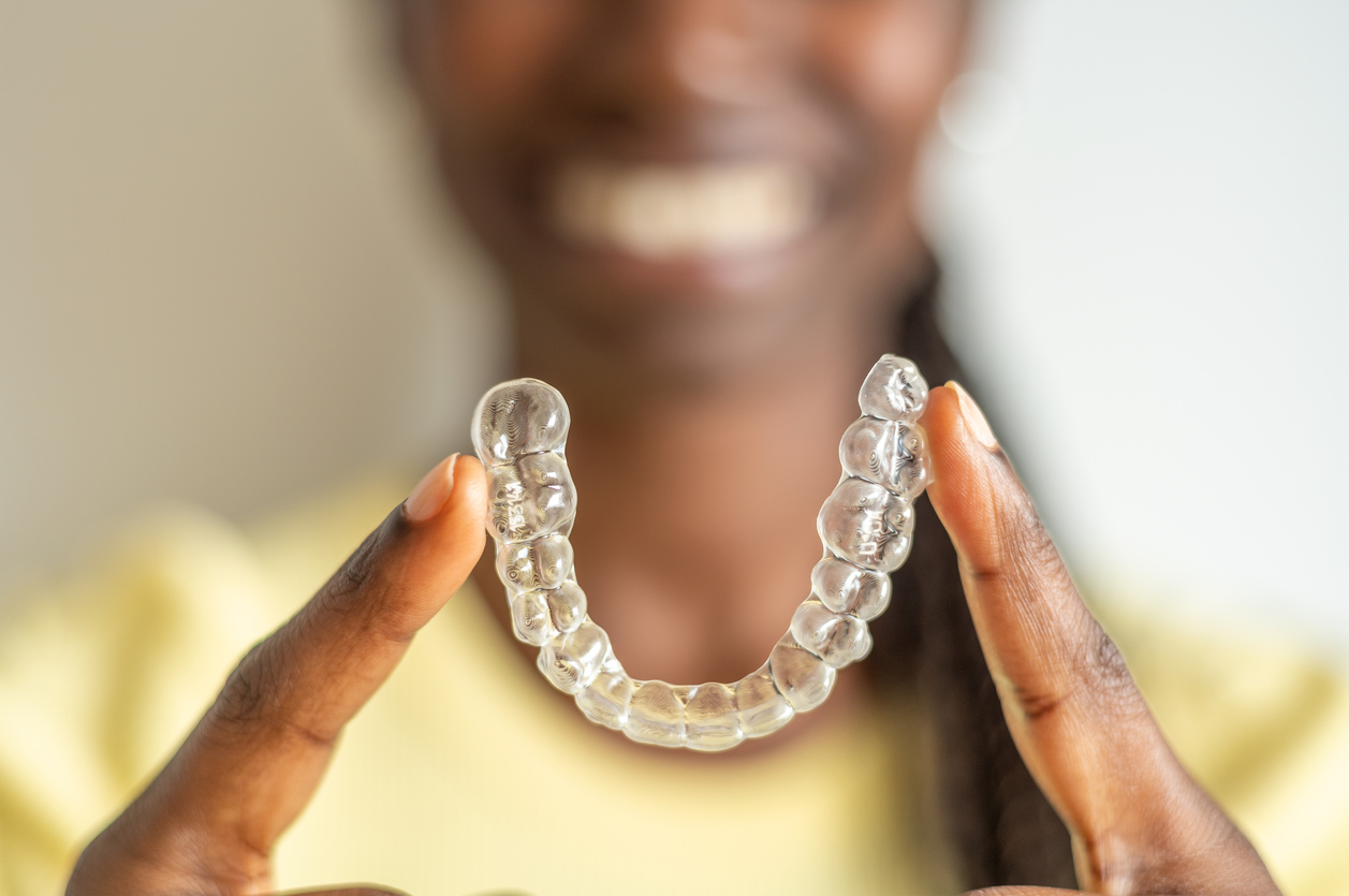 Young woman holding with two fingers an invisible dental aligner while smiling