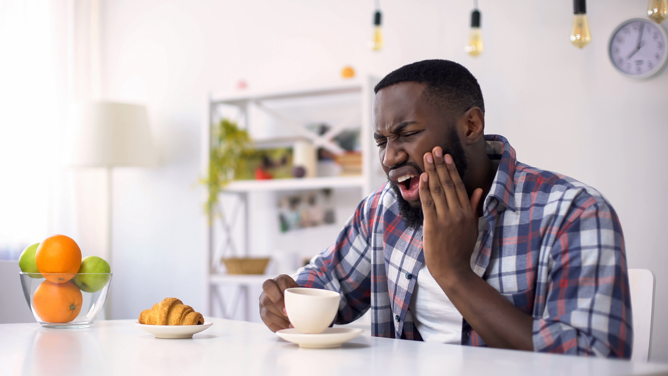 Afro-American man having dental ache, reaction on hot coffee, sensitive teeth