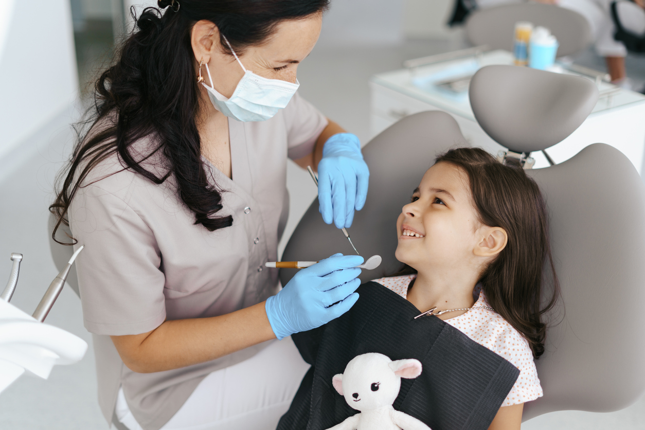 Cute little girl sitting on a modern dental chair and having dental consultation with dentist