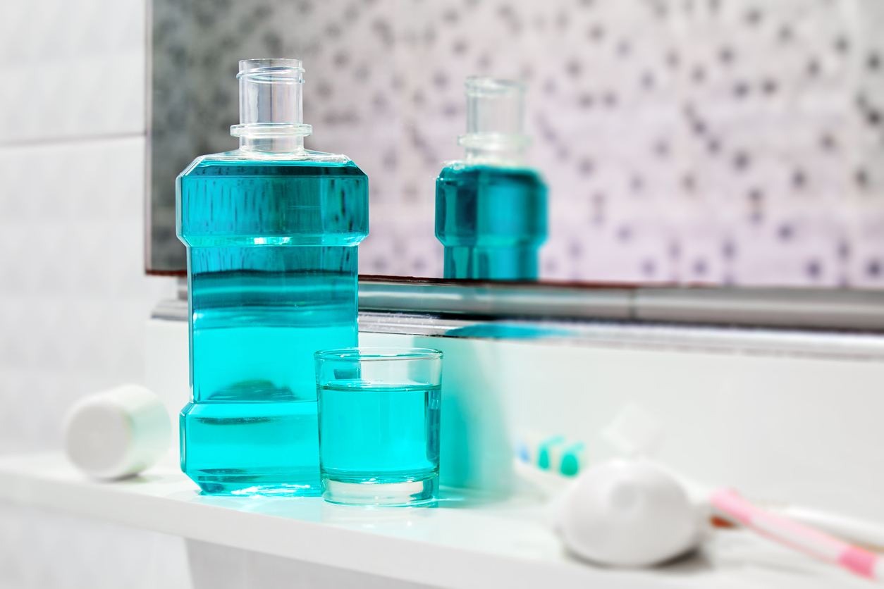 Bottle of mouthwash and glass of mouthwash on bathroom countertop next to mirror